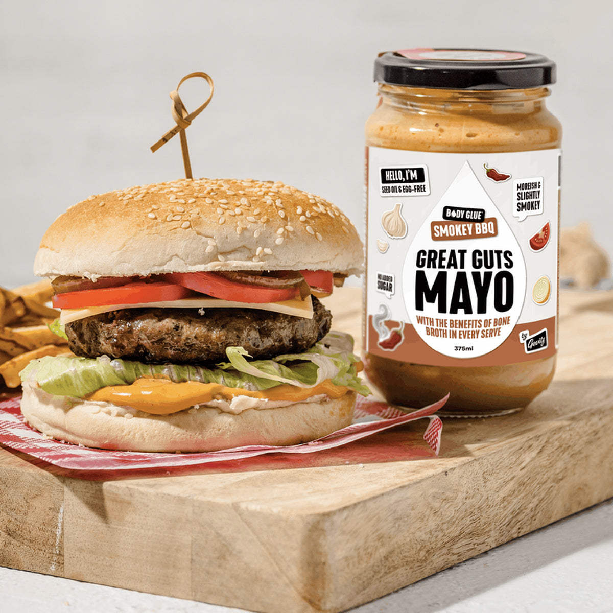 Gevity Great Guts Mayo Smokey BBQ jar beside a burger, full square lifestyle photograph