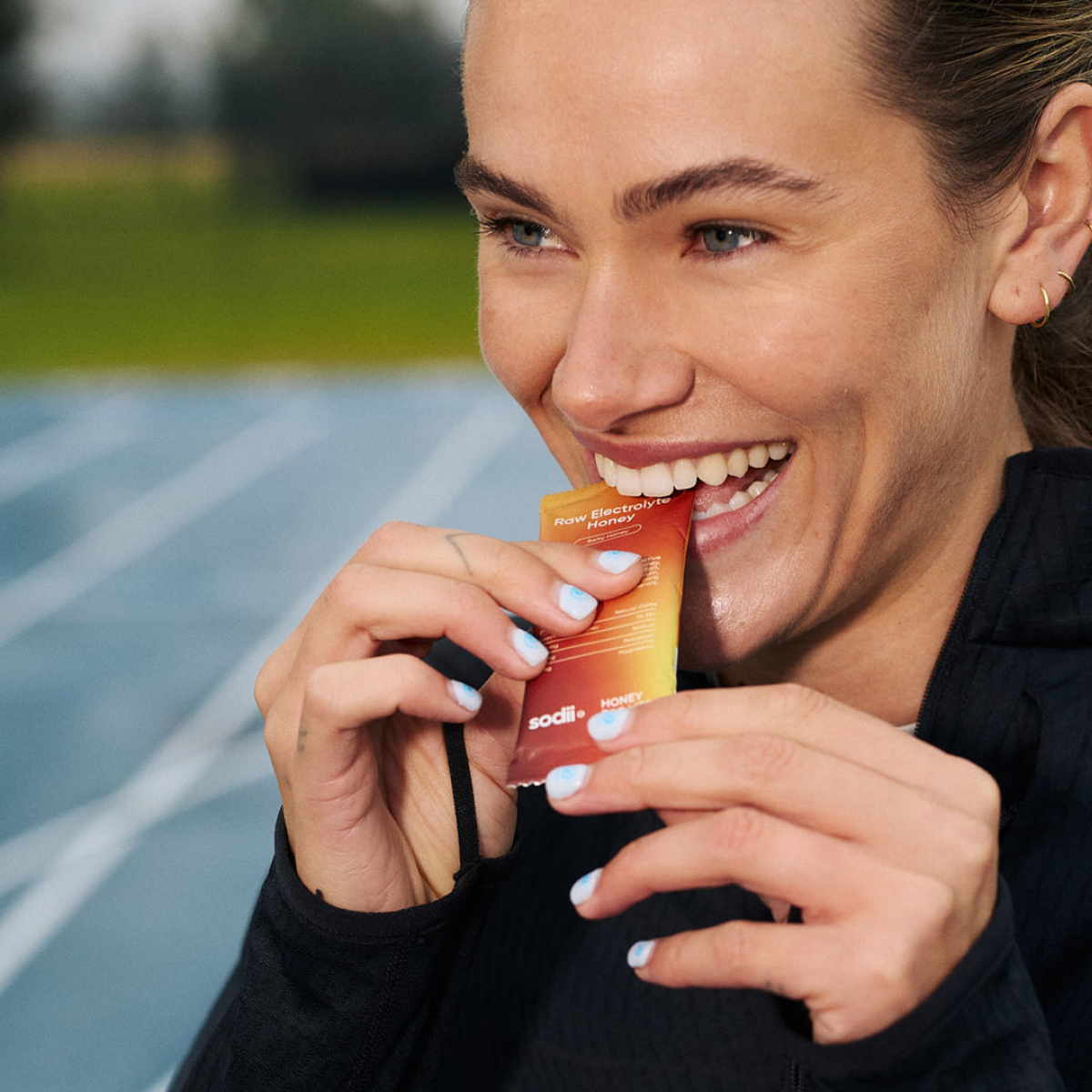 Runner using a Sodii Raw Electrolyte Honey sachet beside a running track